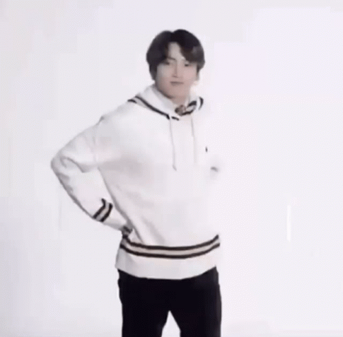 A Young Man In A White Sweater And Black Pants Is Standing With His Hands On His Hips And Smiling . GIF