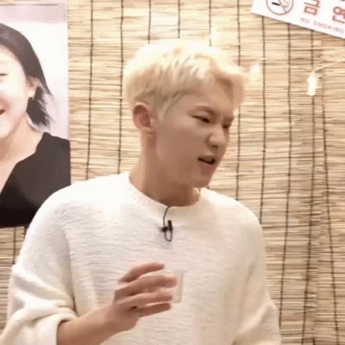A Young Man In A White Sweater Is Holding A Shot Glass In Front Of A No Smoking Sign . GIF