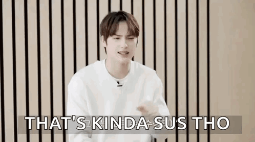 A Young Man In A White Sweater Is Sitting In Front Of A Wooden Wall And Making A Funny Face . GIF