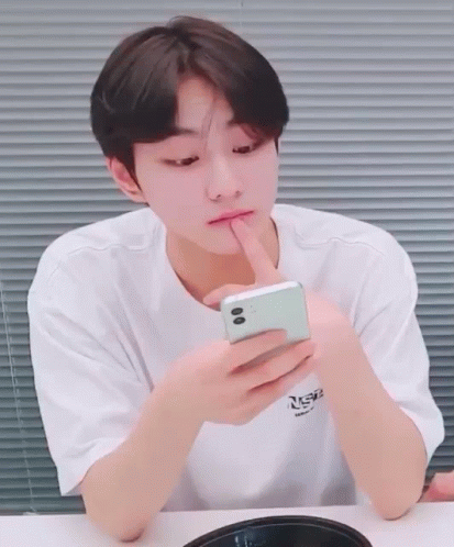 A Young Man In A White T-Shirt Is Looking At A Cell Phone GIF