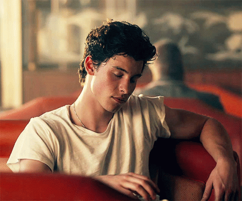 A Young Man In A White T-Shirt Is Sitting In A Red Chair GIF