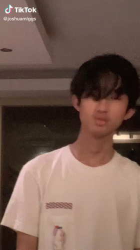 A Young Man In A White T-Shirt Is Standing In A Room . GIF
