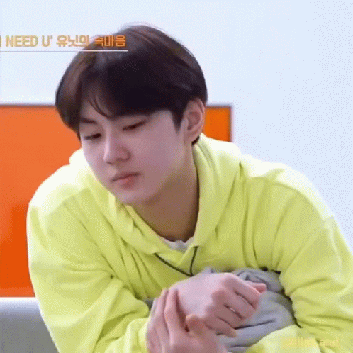 A Young Man In A Yellow Hoodie Is Sitting On A Couch With His Hands Folded . GIF
