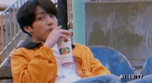 A Young Man In A Yellow Jacket Is Sitting On A Chair Drinking A Cup Of Coffee . GIF