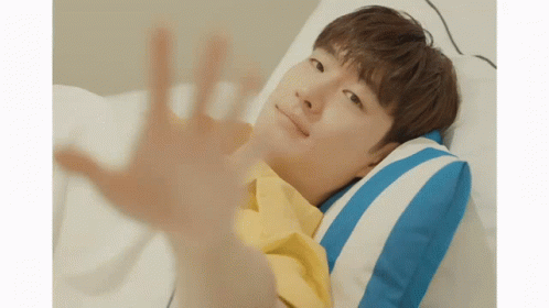 A Young Man In A Yellow Shirt Is Laying In Bed With A Blue And White Striped Pillow GIF