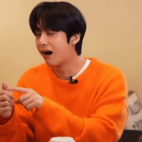 A Young Man In An Orange Sweater Is Sitting At A Table With His Eyes Closed And His Mouth Open . GIF