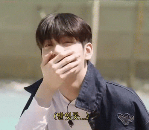 A Young Man Is Covering His Mouth With His Hand And Smiling . GIF