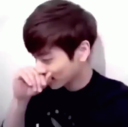 A Young Man Is Covering His Nose With His Hand While Sitting In Front Of A White Wall . GIF