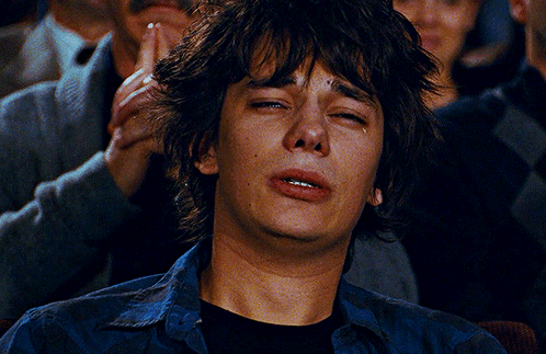 A Young Man Is Crying While Sitting In A Crowd Of People GIF