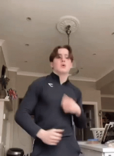 A Young Man Is Dancing In A Living Room While Wearing A Blue Shirt . GIF