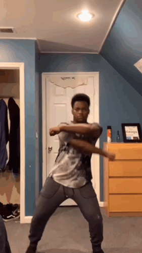 A Young Man Is Dancing In A Room With A Blue Wall And A Dresser . GIF