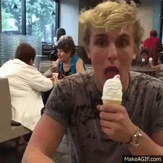 A Young Man Is Eating An Ice Cream Cone In A Restaurant While Sitting At A Table . GIF