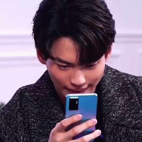 A Young Man Is Holding A Blue Cell Phone In His Hand And Looking At It . GIF
