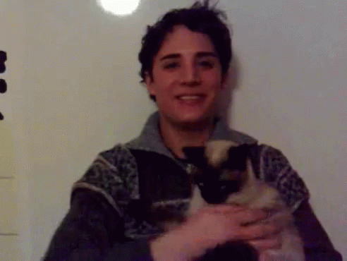 A Young Man Is Holding A Cat In His Arms And Smiling GIF