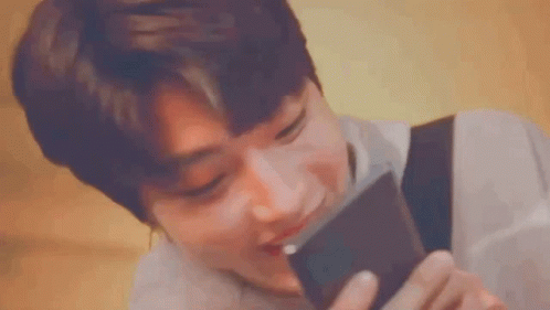 A Young Man Is Holding A Cell Phone In His Hand And Smelling It . GIF