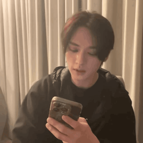 A Young Man Is Holding A Cell Phone In His Hand . GIF