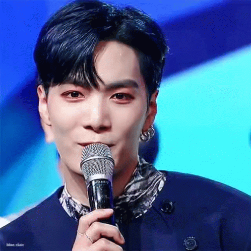 A Young Man Is Holding A Microphone In His Hand And Talking Into It . GIF