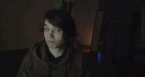 A Young Man Is Holding A Piece Of Paper And A Pen In A Dark Room . GIF