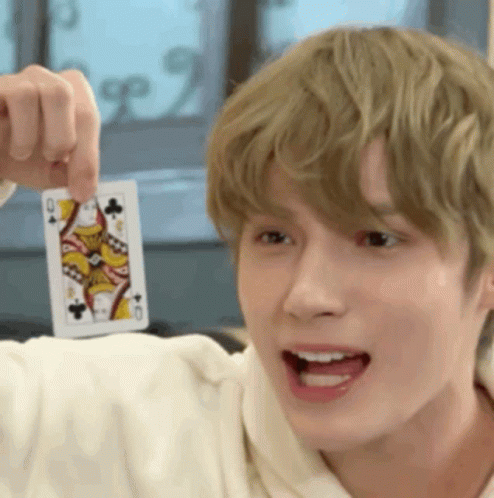 a young man is holding a playing card in his hand and pointing it at the camera .