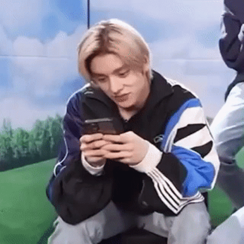 A Young Man Is Kneeling Down While Looking At His Cell Phone . GIF
