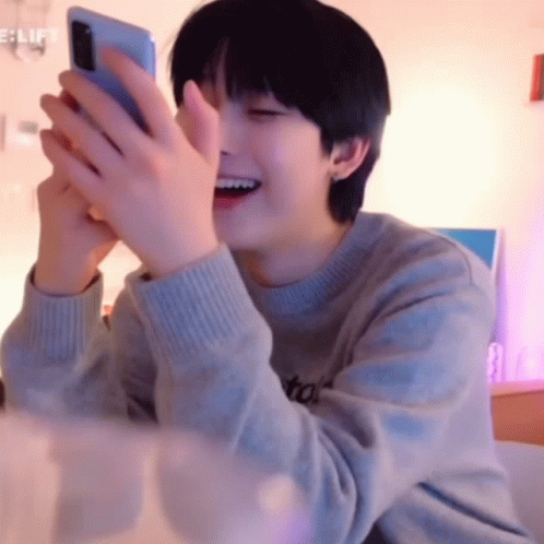 A Young Man Is Laughing While Holding A Cell Phone . GIF