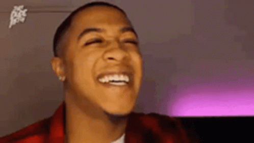 a young man is laughing with his eyes closed and wearing a red plaid jacket .