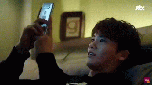 A Young Man Is Laying On A Bed Looking At His Cell Phone . GIF