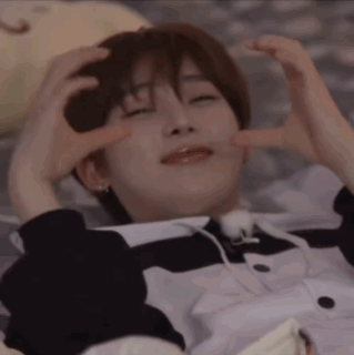 A Young Man Is Laying On A Bed With His Eyes Closed And Making A Heart Shape With His Hands . GIF