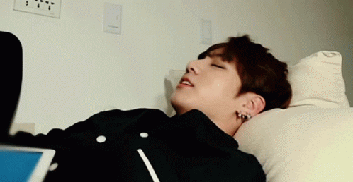 A Young Man Is Laying On A Bed With His Head On A Pillow GIF