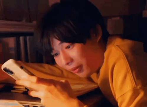 A Young Man Is Laying On His Stomach Looking At His Cell Phone . GIF