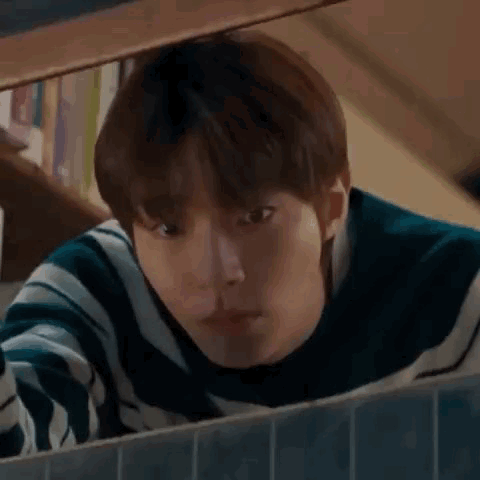 A Young Man Is Looking Out Of A Window . GIF