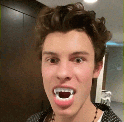A Young Man Is Making A Funny Face With Fake Vampire Teeth . GIF