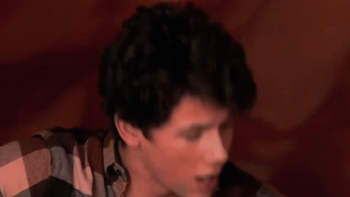 A Young Man Is Playing A Guitar In Front Of A Large Red Object GIF