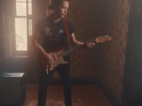 A Young Man Is Playing An Electric Guitar In A Dark Room . GIF