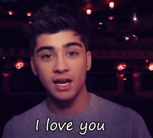A Young Man Is Saying I Love You In Front Of A Dark Background GIF
