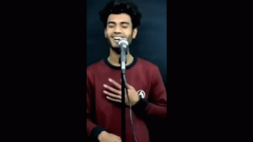 A Young Man Is Singing Into A Microphone While Holding His Hand To His Chest . GIF