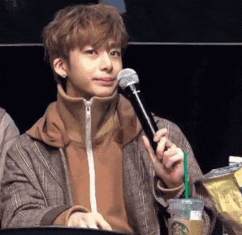 A Young Man Is Sitting At A Table Holding A Microphone And A Cup Of Starbucks Coffee . GIF