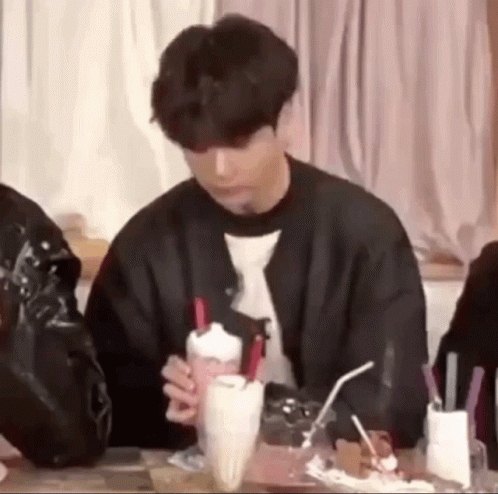 A Young Man Is Sitting At A Table Holding A Milkshake With Straws . GIF