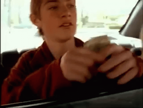 a young man is sitting in a car holding a bunch of money .