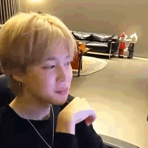 A Young Man Is Sitting In A Chair In A Living Room With His Hand On His Shoulder . GIF