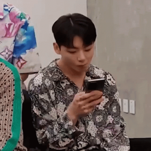 a young man is sitting in a chair looking at his cell phone .