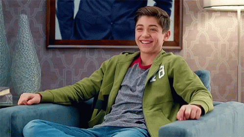 A Young Man Is Sitting In A Chair Smiling . GIF