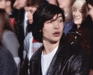 A Young Man Is Sitting In A Crowd Of People Wearing A Leather Jacket . GIF