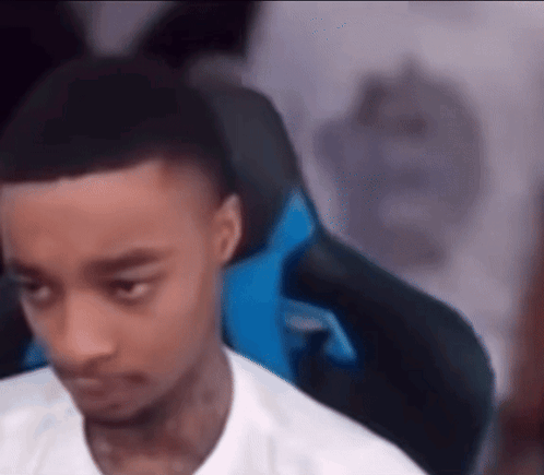 A Young Man Is Sitting In A Gaming Chair Looking At The Camera . GIF