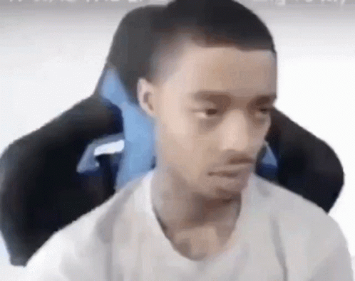 A Young Man Is Sitting In A Gaming Chair With A Blue Pillow . GIF