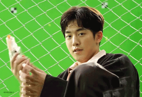 A Young Man Is Sitting In Front Of A Chain Link Fence Holding A Bottle Of Water . GIF