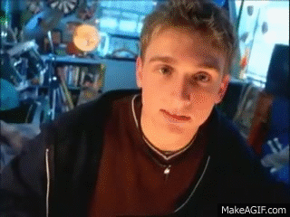 A Young Man Is Sitting In Front Of A Computer Screen And Looking At The Camera While Wearing A Necklace . GIF
