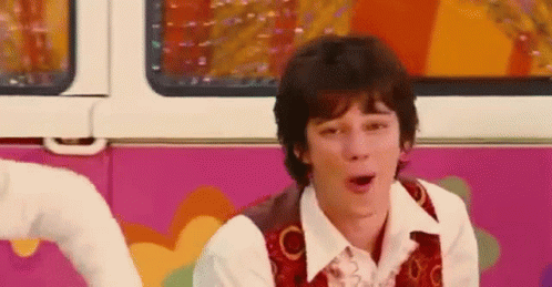 A Young Man Is Sitting In Front Of A Pink And White Van . GIF