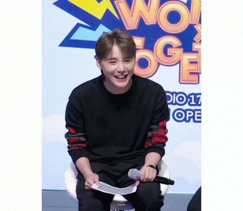 A Young Man Is Sitting In Front Of A Sign That Says Wow Oge GIF