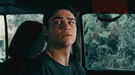 A Young Man Is Sitting In The Back Seat Of A Car Looking At The Camera . GIF